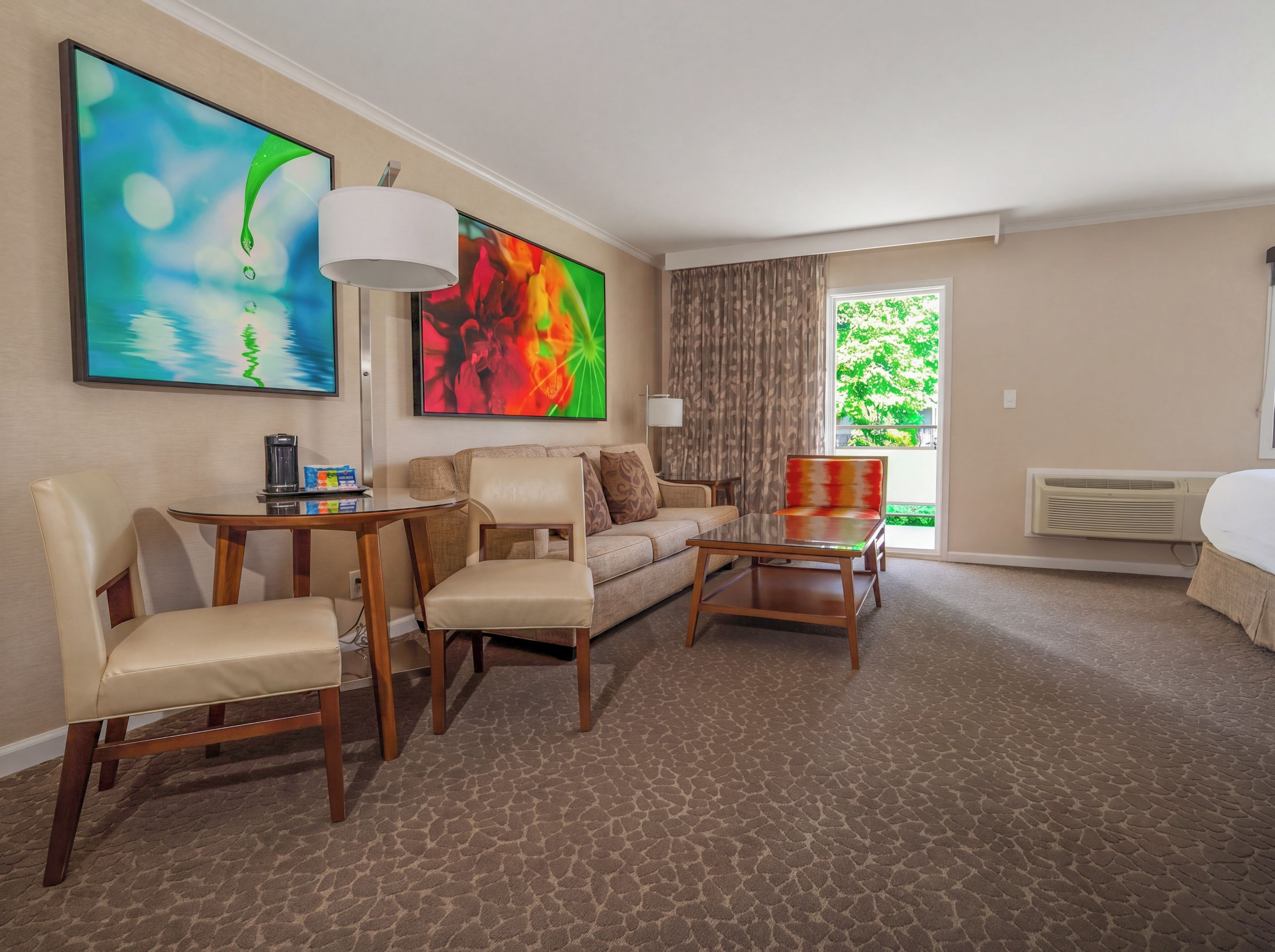 A hotel room with a sofa, two armchairs, a coffee table, a TV, and a window with curtains.