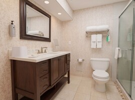 A bathroom with a wooden vanity, a toilet, a glass shower enclosure, and a towel rack with multiple towels.