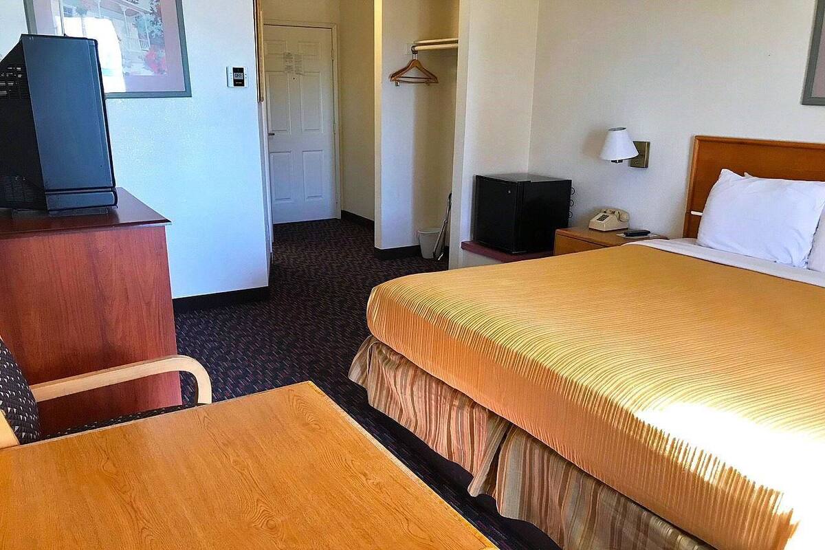 A hotel room with a bed, a desk, a chair, a television, a telephone, and a coat rack.