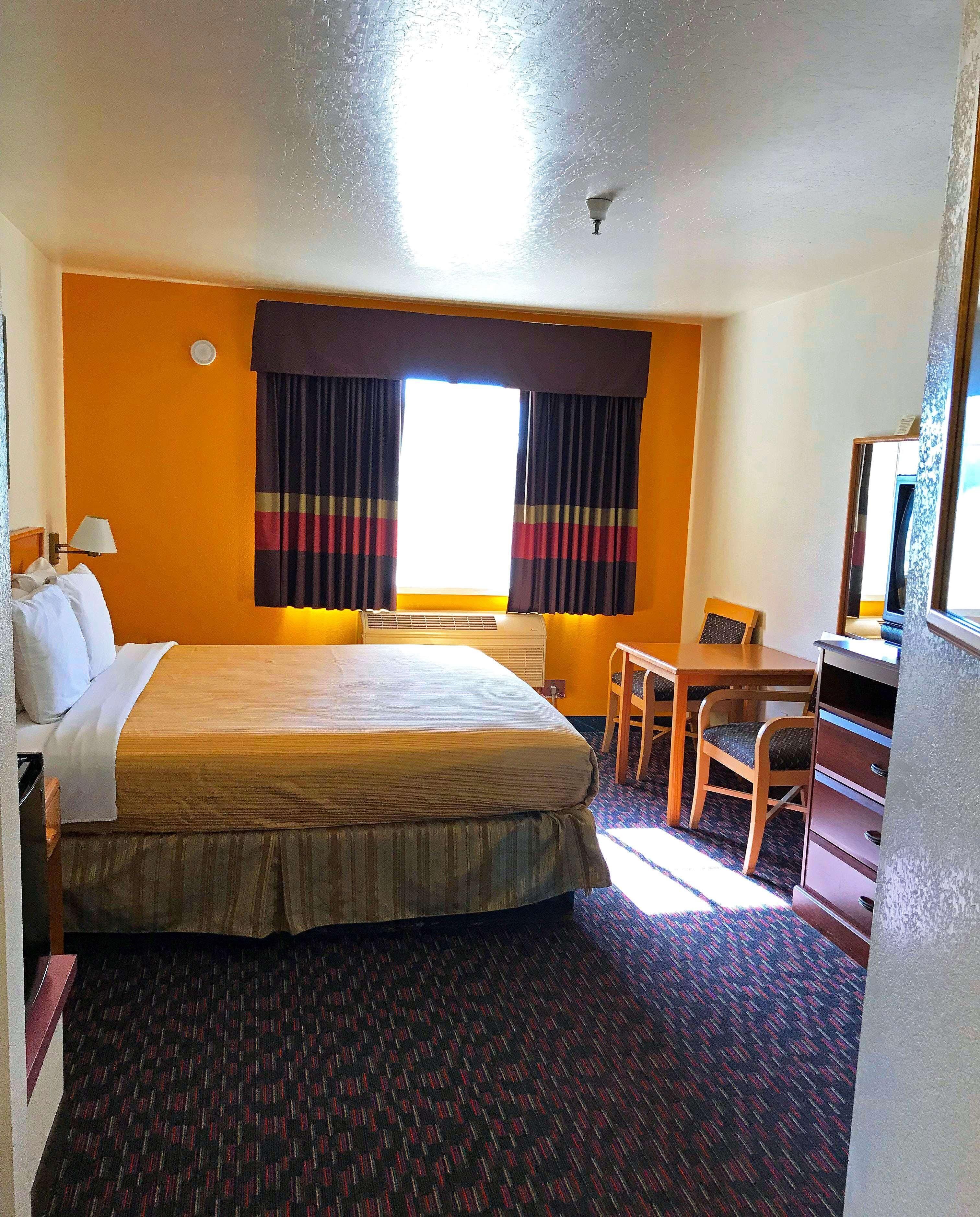 A hotel room with a large bed, a desk, a chair, a lamp, and a window with curtains.