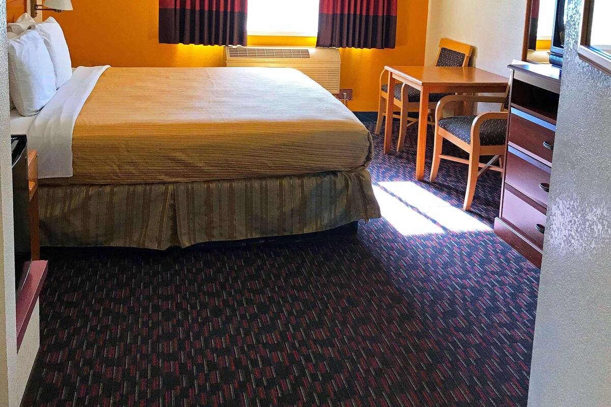 A hotel room with a large bed, a desk, a chair, a lamp, and a window with curtains.