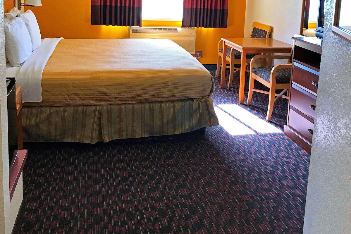 A hotel room with a large bed, a desk, a chair, a lamp, and a window with curtains.