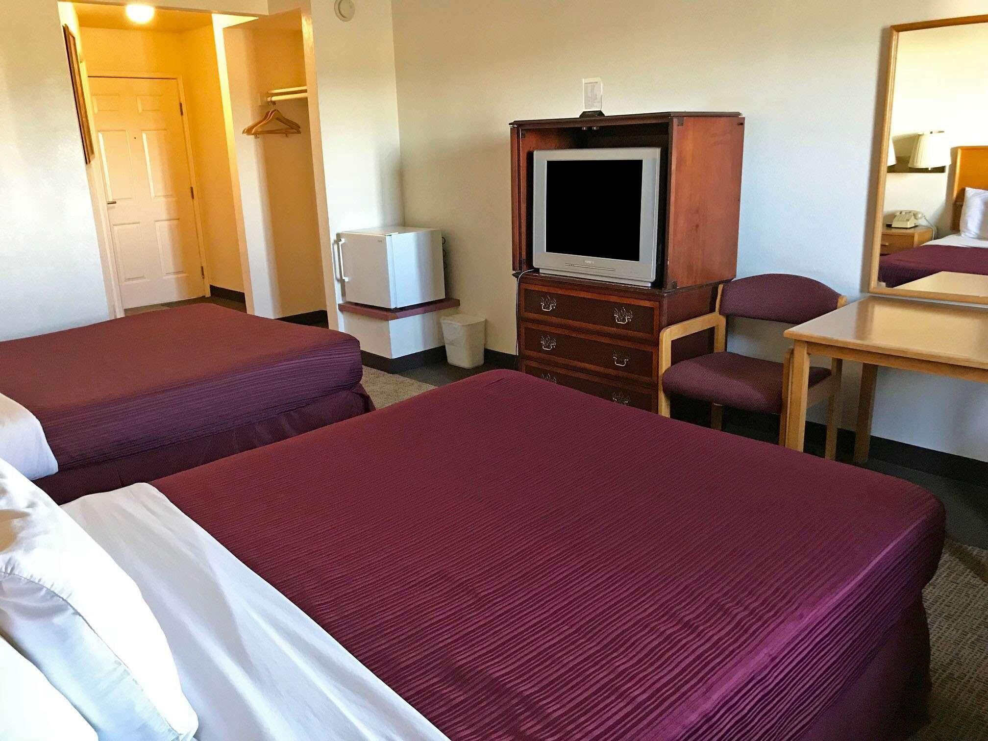 A hotel room with two beds, a television, a small refrigerator, a wooden dresser, and a desk with a chair.