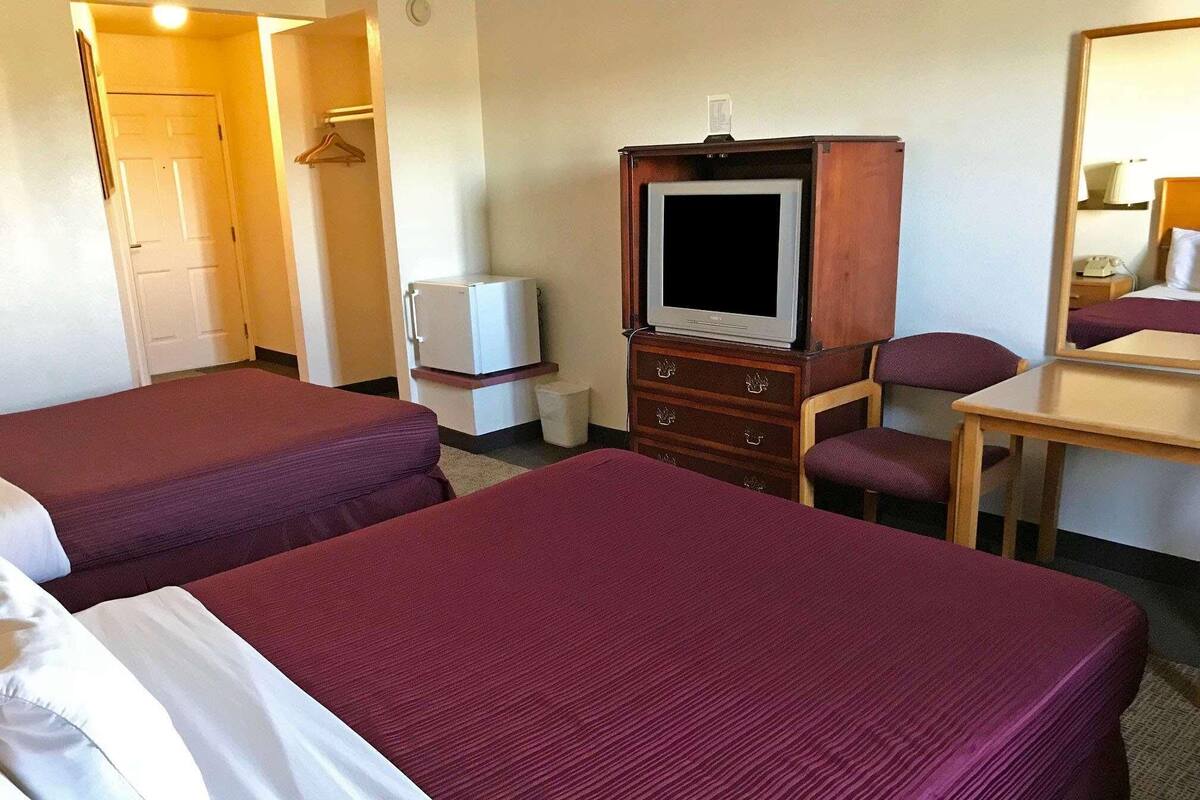 A hotel room with two beds, a television, a small refrigerator, a wooden dresser, and a desk with a chair.
