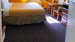 Hotellihuone, jossa on suuri sänky, työpöytä, tuoli, lamppu ja ikkuna, jossa on verhot.