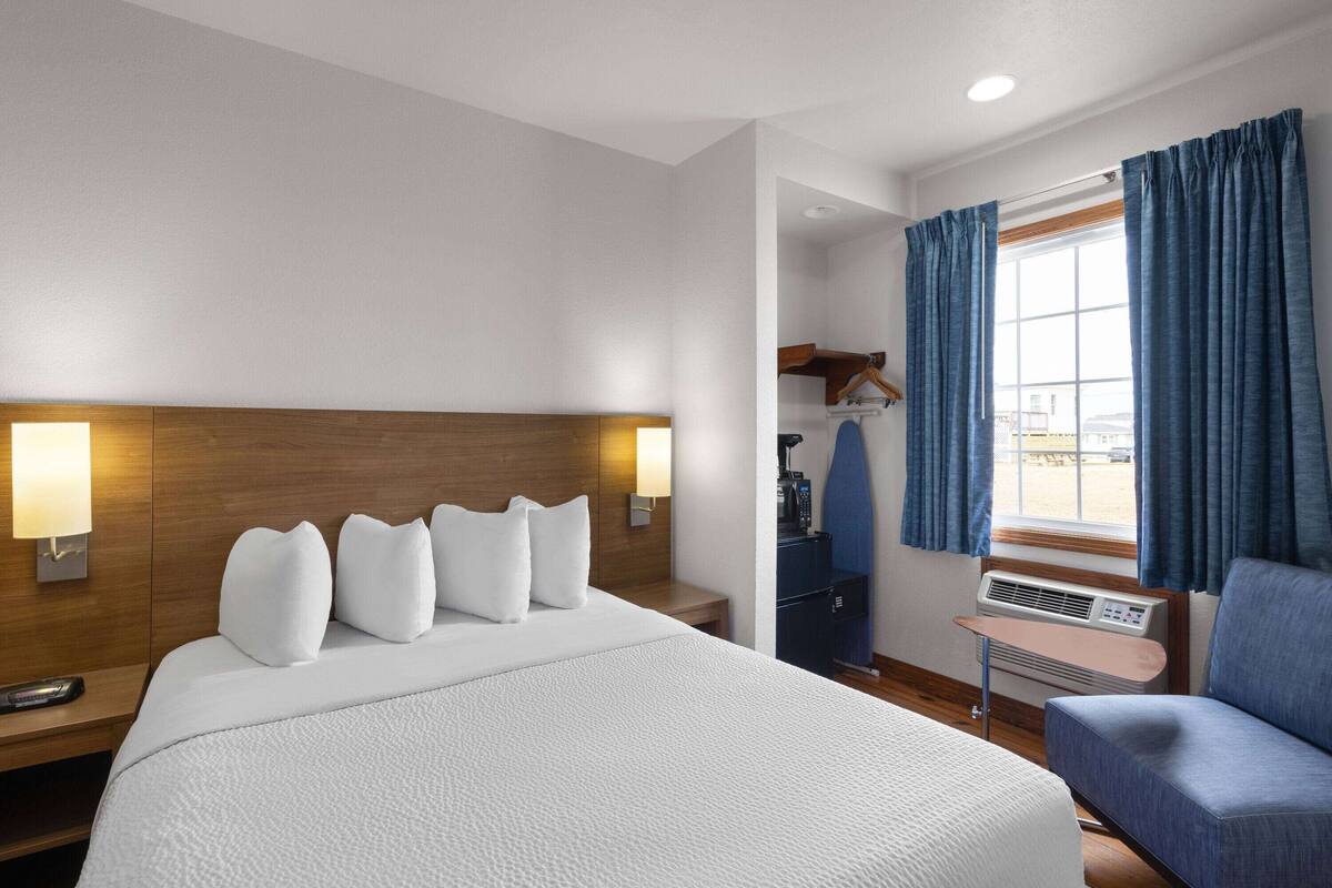 A hotel room with a large bed, bedside lamps, a small table, a chair, and a window with curtains.