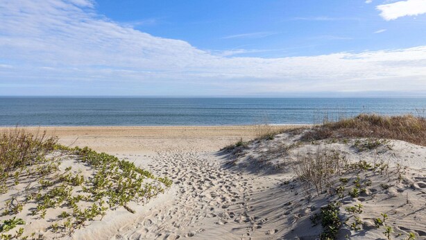 A sandy beach with footprints and sparse vegetation, leading to a calm sea under a clear sky. - Days Inn by Wyndham Kill Devil Hills Oceanfront - Wilbur (Kill Devil Hills)