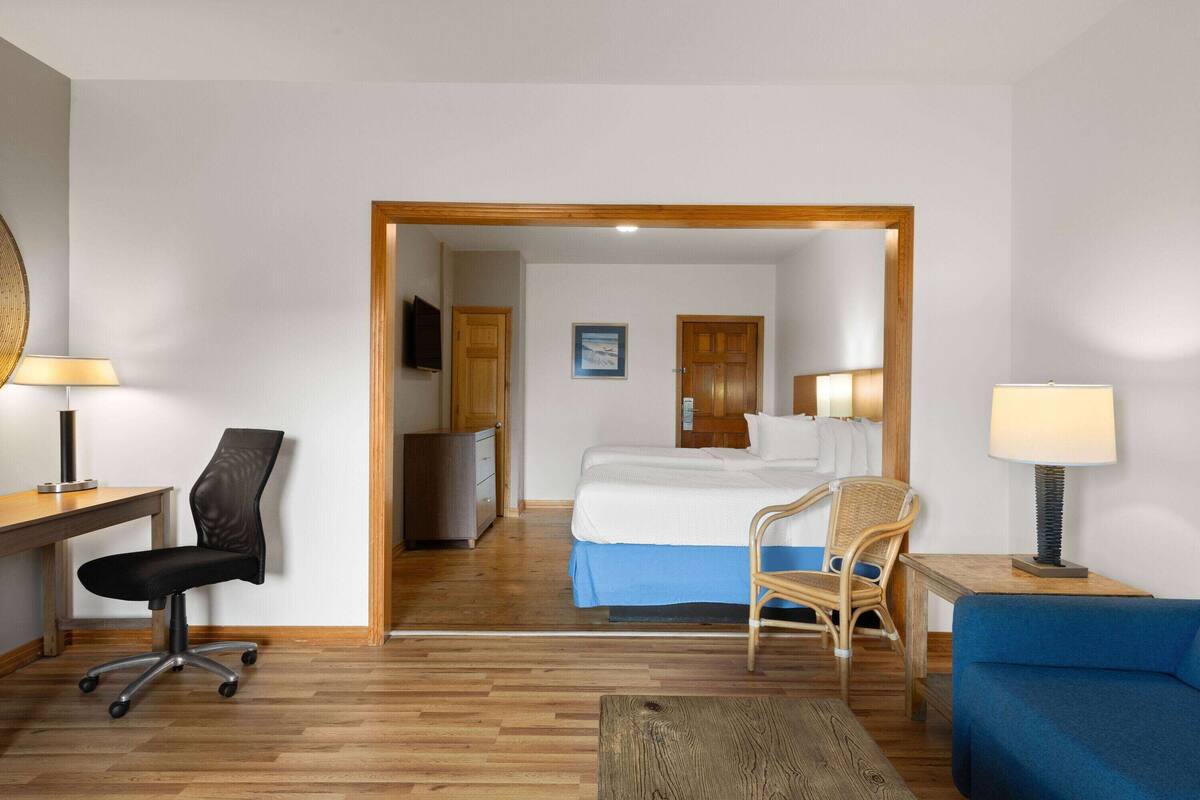 A hotel room with a bed, a desk with a chair, a blue sofa, and a wooden floor.