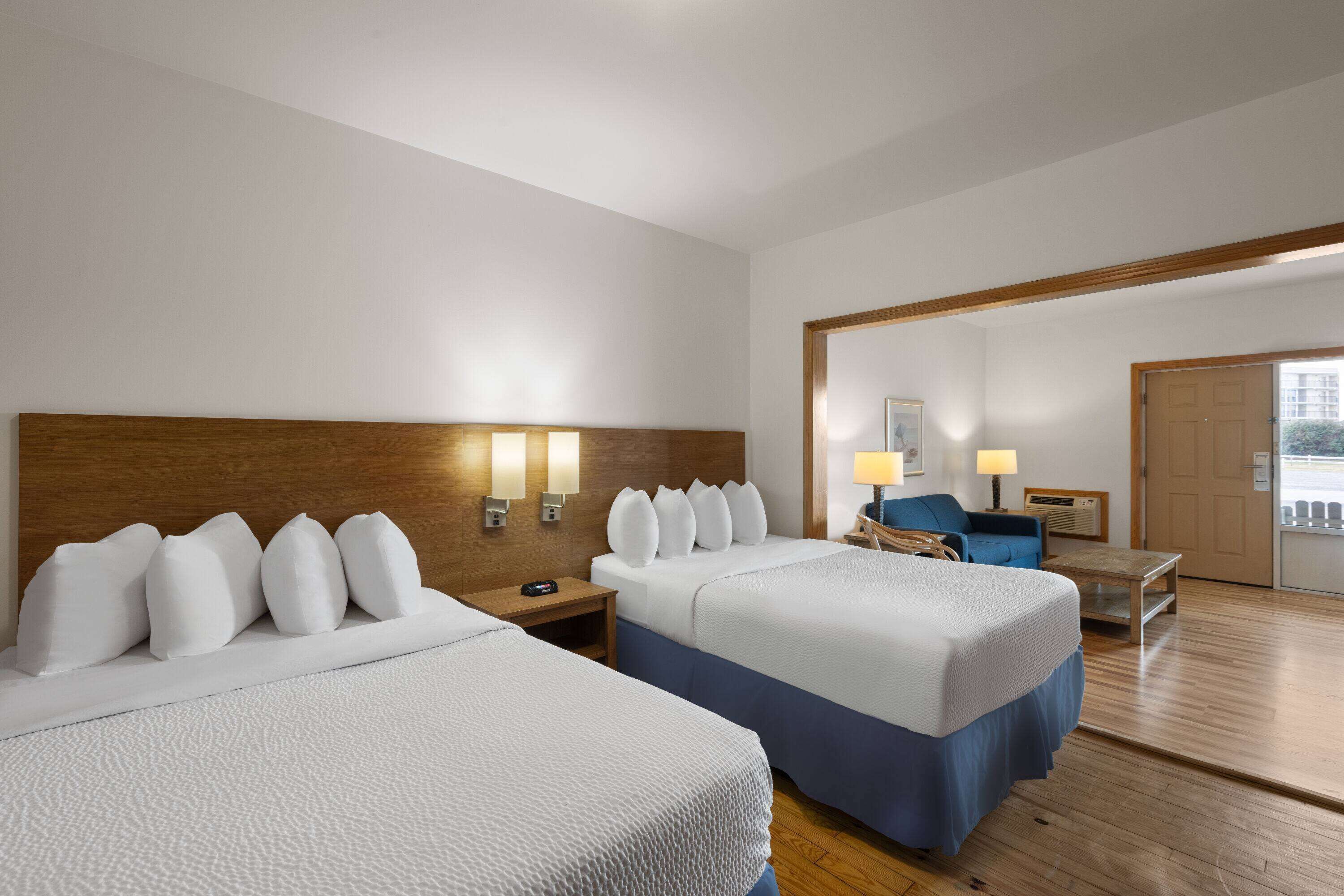 A hotel room with two beds, a wooden headboard, bedside lamps, a desk, and a chair.