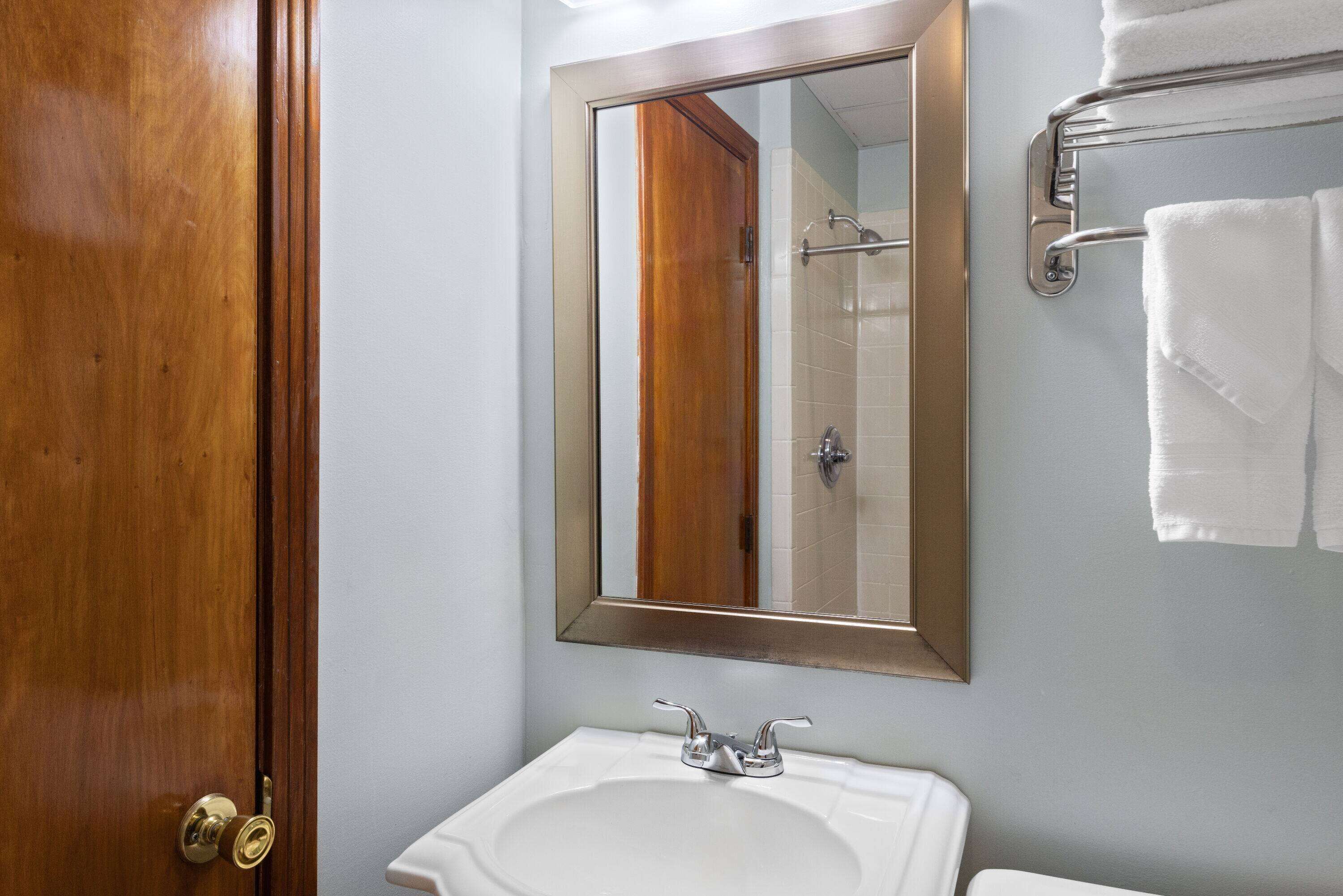 A bathroom with a wooden door, a white sink, a mirror, and a towel rack.