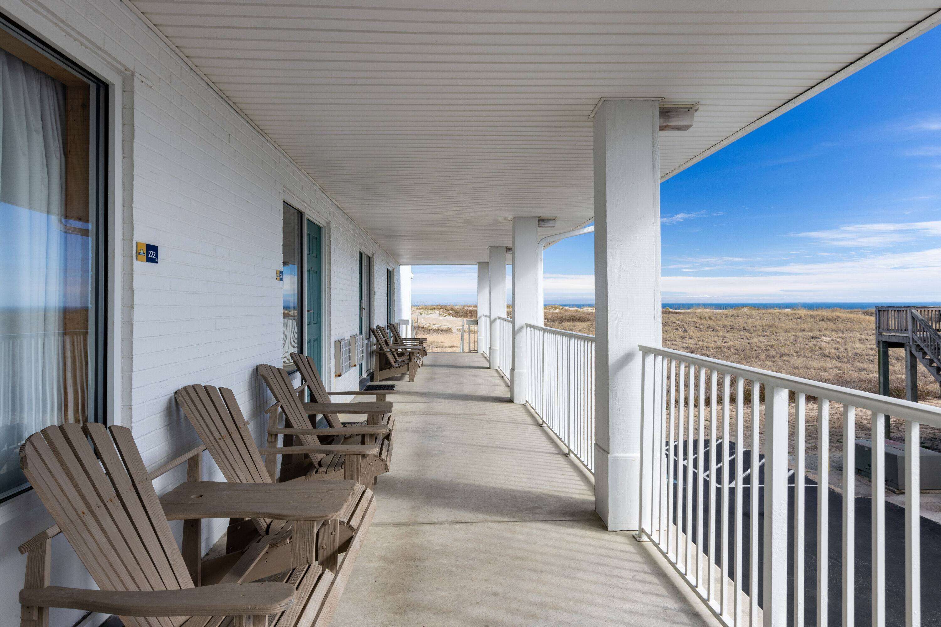Une véranda couverte avec des chaises en bois et vue sur la plage.