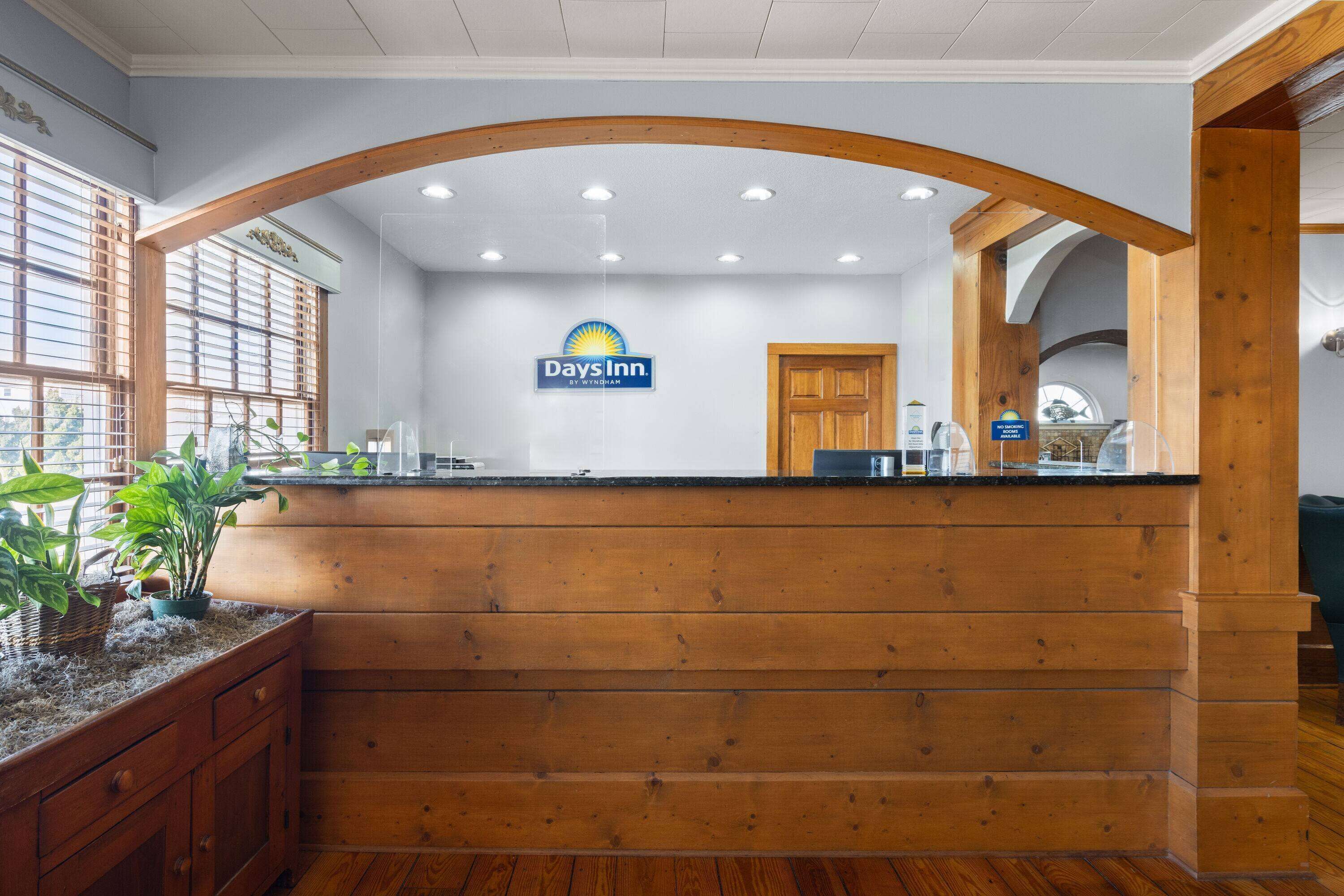 A reception area with a wooden counter, a sign for Days Inn, and a window with blinds.
