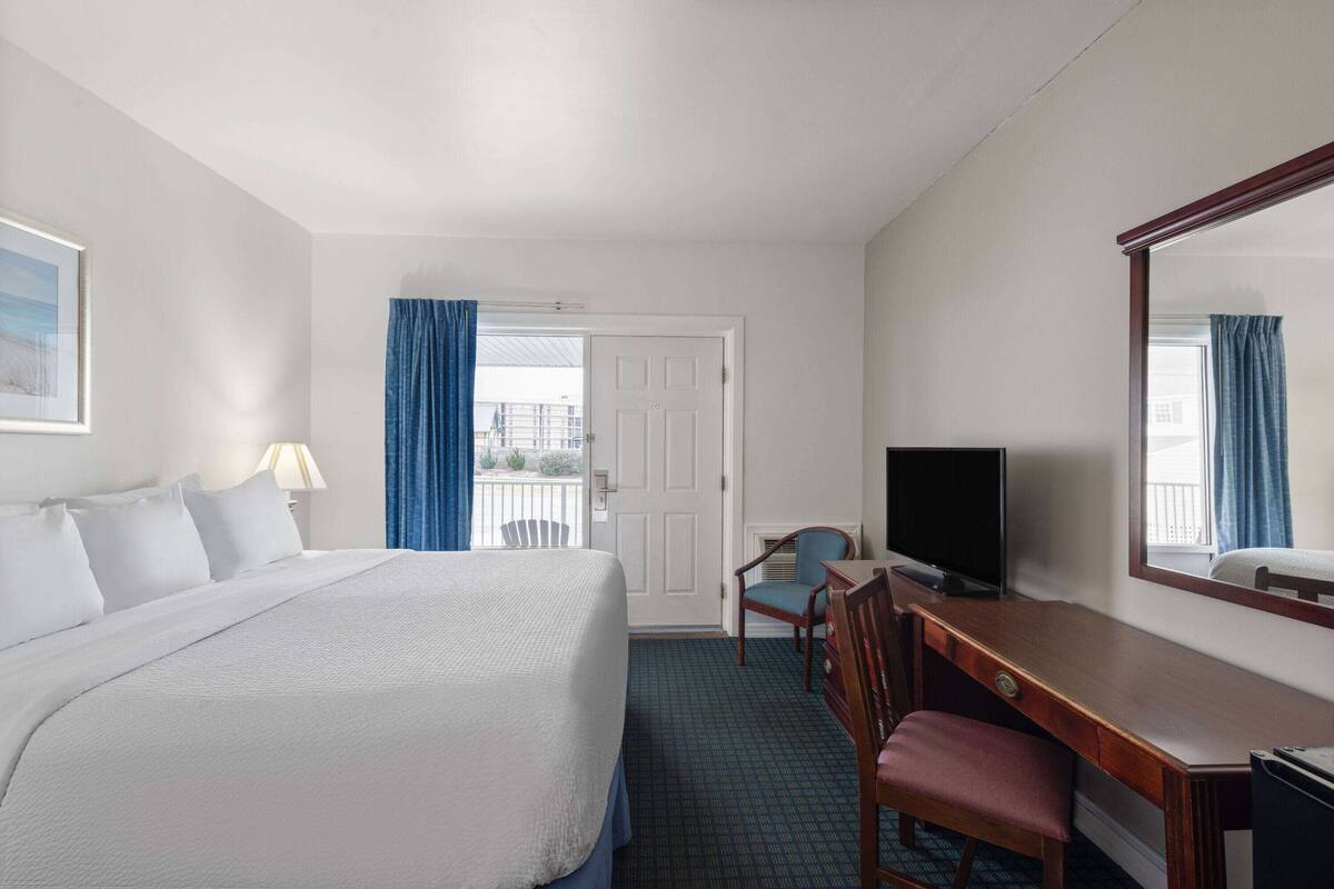 A hotel room with a large bed, a desk with a chair, a television, and a window with curtains.