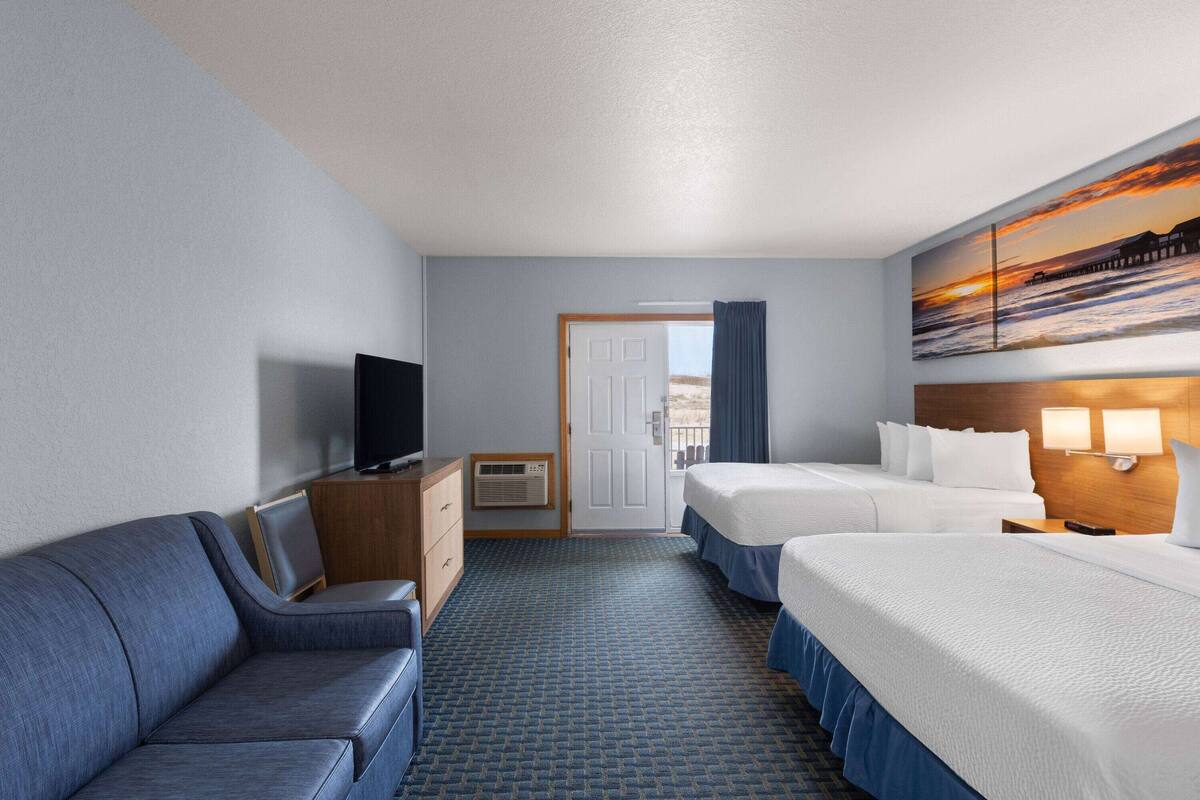 A hotel room with a sofa, two beds, a TV, a painting, and a door leading to a balcony.