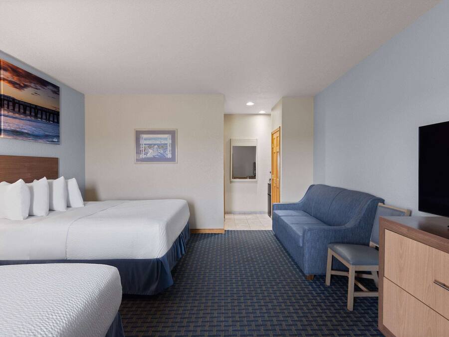 A hotel room with two beds, a sofa, a TV, and a small desk.