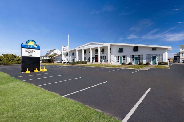 A Days Inn with a clear sky, a parking lot, and a building with a white facade and green doors.