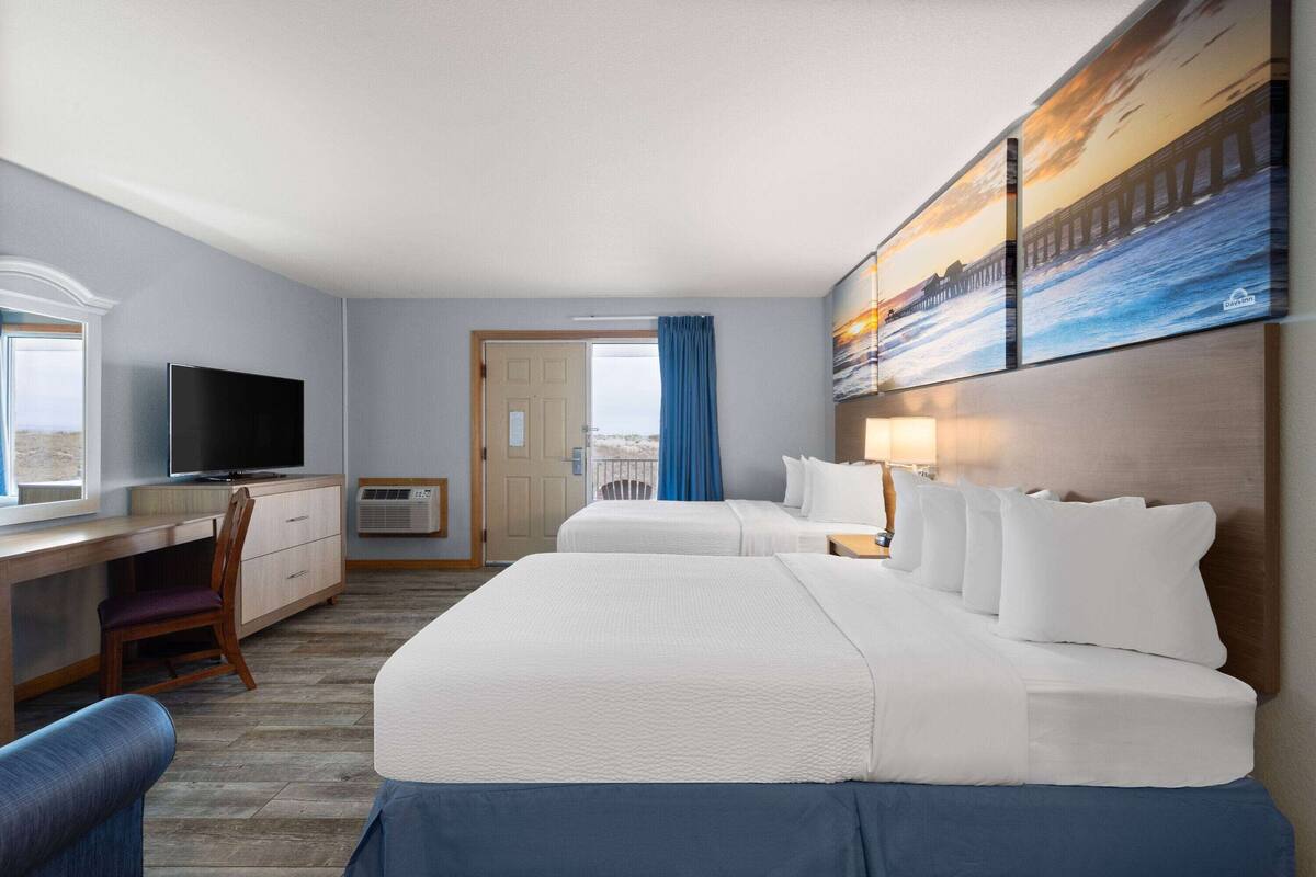 Habitación de hotel con dos camas, un escritorio, un televisor y un amplio ventanal con vistas al exterior.
