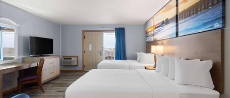 A hotel room with two beds, a desk, a TV, and a large window with a view of the outdoors.
