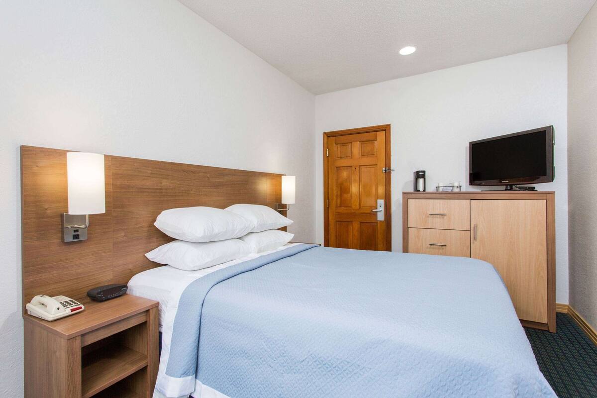 A hotel room with a bed, bedside table with a phone, a TV, and a wooden wardrobe.
