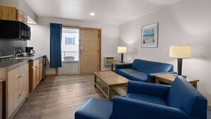 A compact living space with a kitchenette, a blue sofa, a wooden coffee table, and a small side table with a lamp. - Days Inn by Wyndham Kill Devil Hills Oceanfront - Wilbur (Kill Devil Hills)