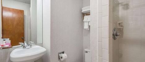 Une salle de bain avec un lavabo, des toilettes et une douche, le tout de couleur blanche.