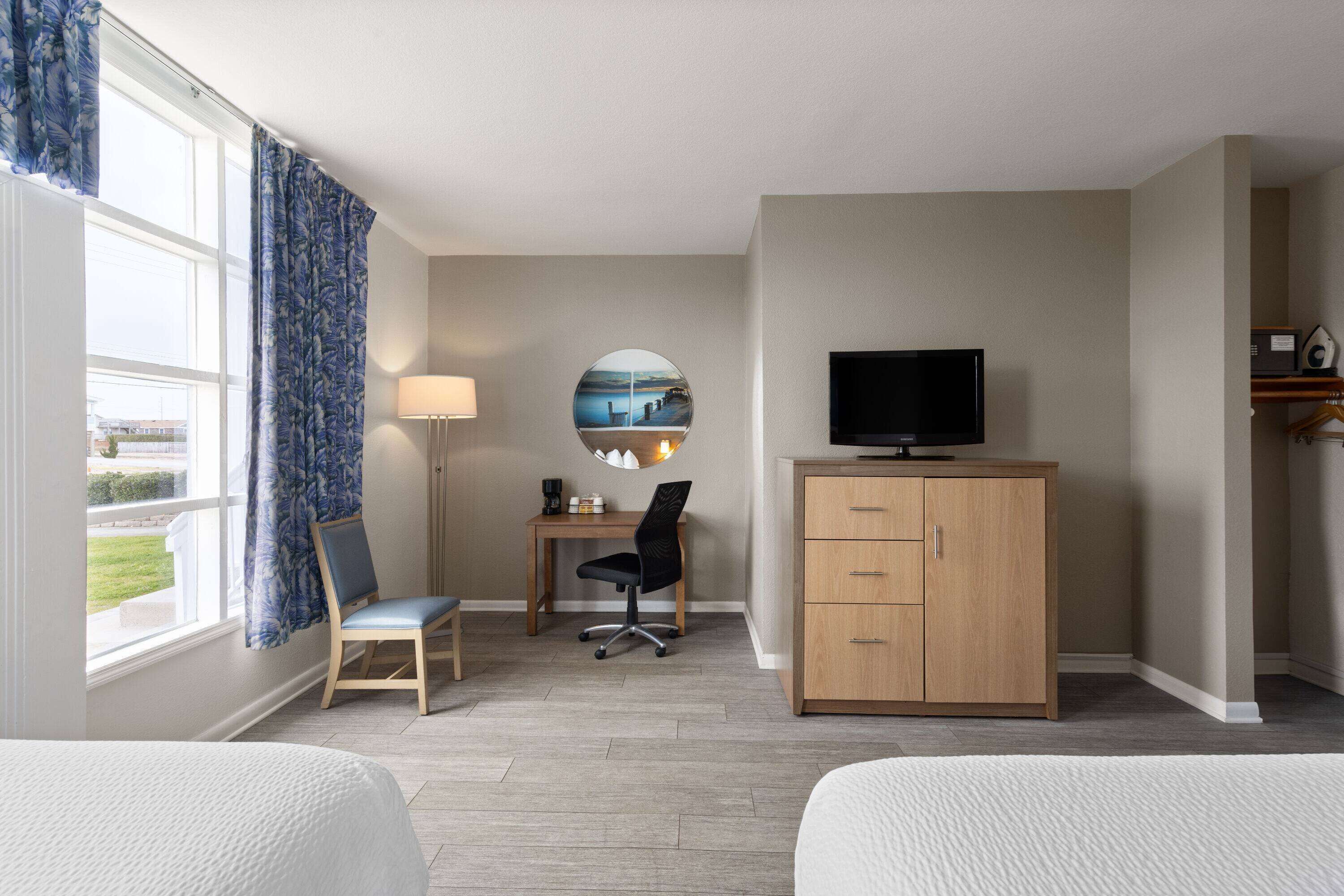 Una habitación de hotel con una cama, un escritorio con una silla, un televisor y un armario.