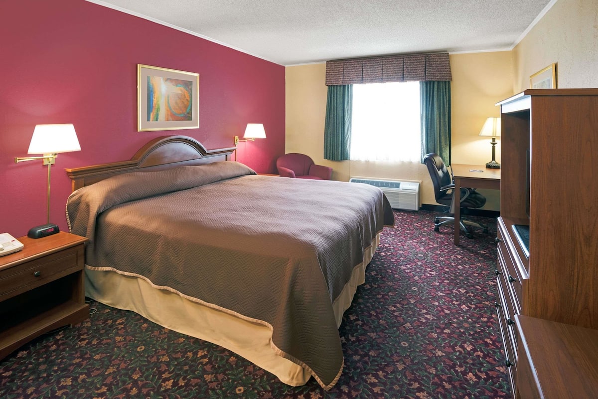 A hotel room with a large bed, a desk, a chair, a lamp, and a window with curtains.