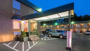 A hotel entrance with a covered walkway, a parking area, and a building with multiple windows and balconies. - Travelodge by Wyndham Beckley (Beckley)