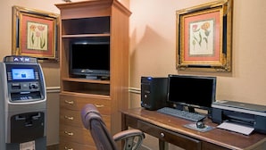 A hotel room with a desk, computer, printer, and ATM. There are framed floral pictures on the wall and a wooden cabinet with a television. - Travelodge by Wyndham Beckley (Beckley)