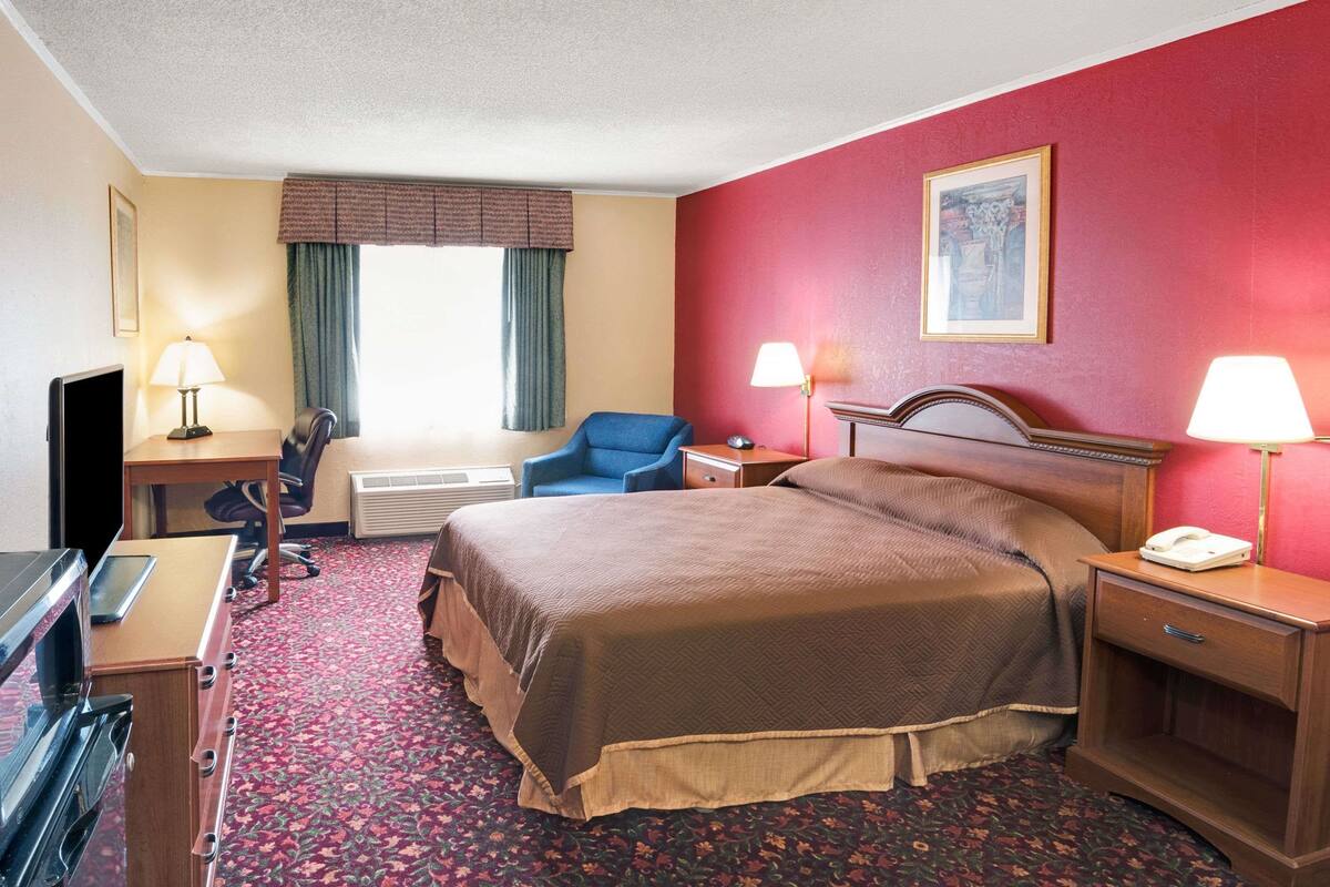 A hotel room with a bed, desk, chair, and a television.