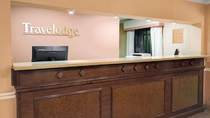 A reception desk with a 'Travelodge' sign, a Lenovo computer, and a bulletin board with various notices. - Travelodge by Wyndham Beckley (Beckley)