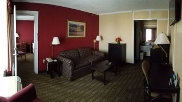 A hotel room with a red wall, a brown leather sofa, a small table, a lamp, a desk with a computer, and a painting.