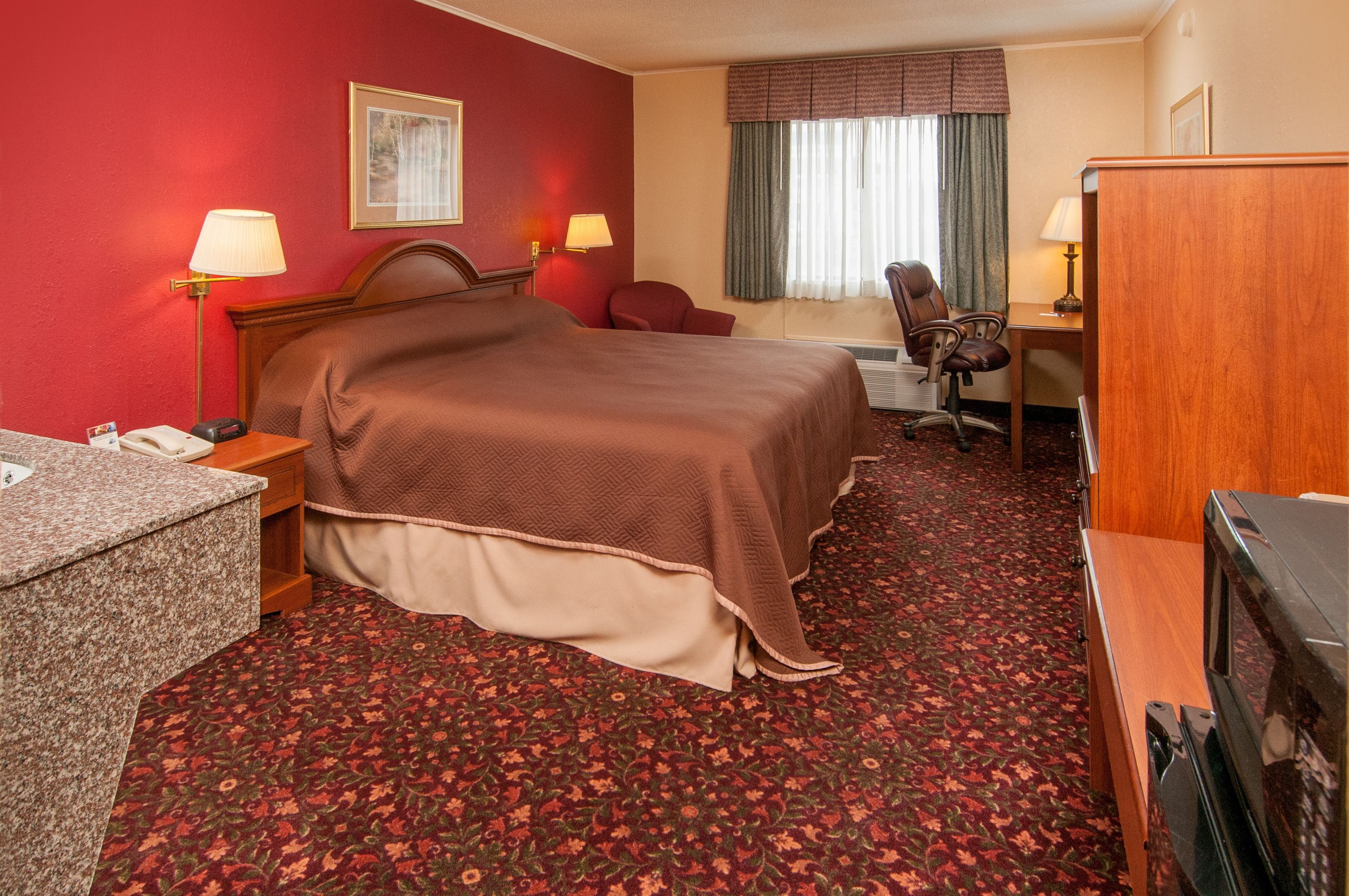 Una habitación de hotel con cama, escritorio, silla y televisor.