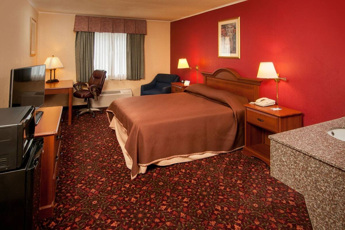 A hotel room with a bed, desk, television, and a bathroom.