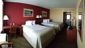 Two single beds with white linens, a desk, and a chair in a cozy room with a bathroom area.