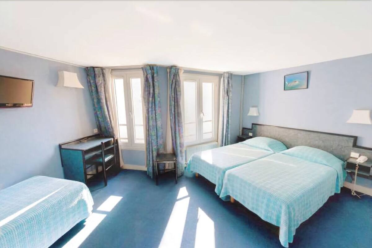 A hotel room with two beds, a desk, a chair, a TV, and a window with curtains.