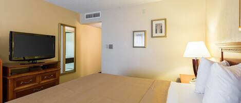 A hotel room with a bed, a television on a wooden dresser, a nightstand with a lamp, and framed pictures on the wall.
