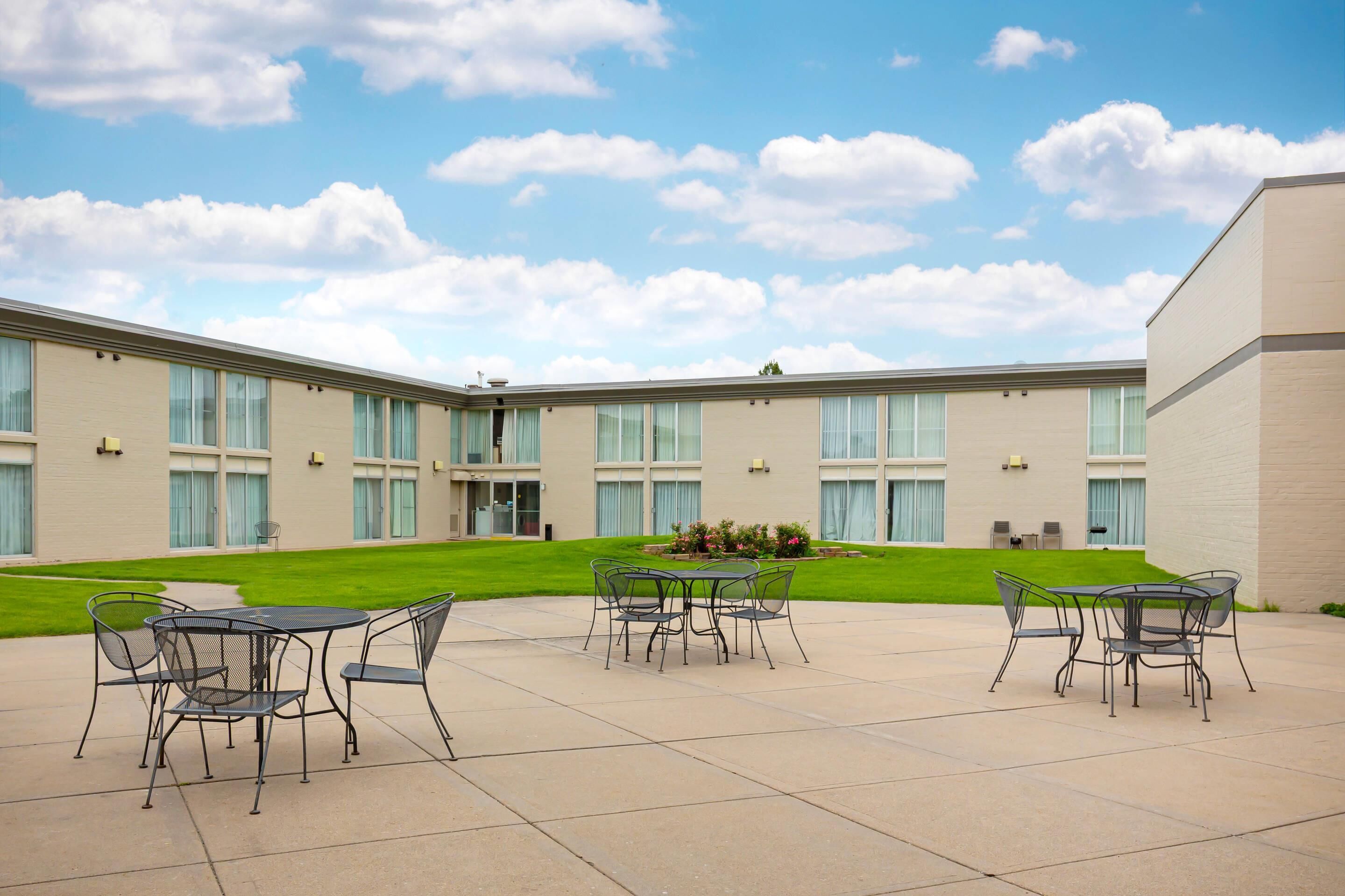A courtyard with outdoor seating, a building with large windows, and a well-maintained lawn.