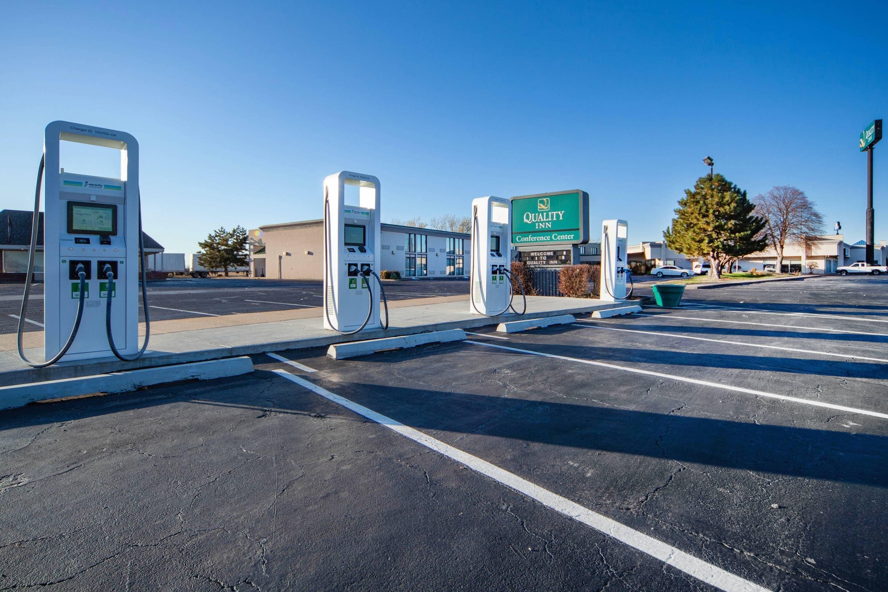 Un estacionamiento con estaciones de carga para vehículos eléctricos, un cartel del Quality Inn Conference Center y un edificio al fondo.