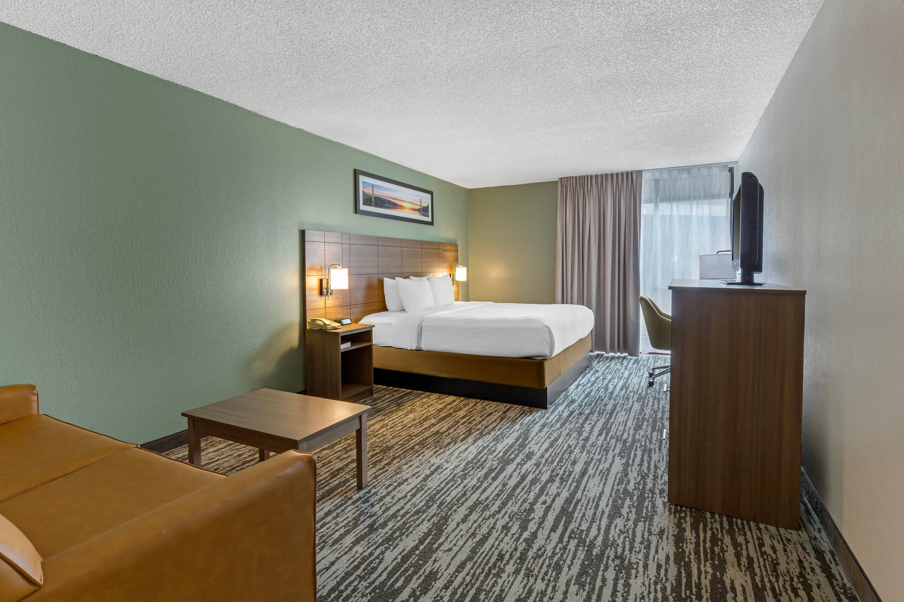 A hotel room with a bed, bedside table, lamp, desk, chair, and a television on a stand.