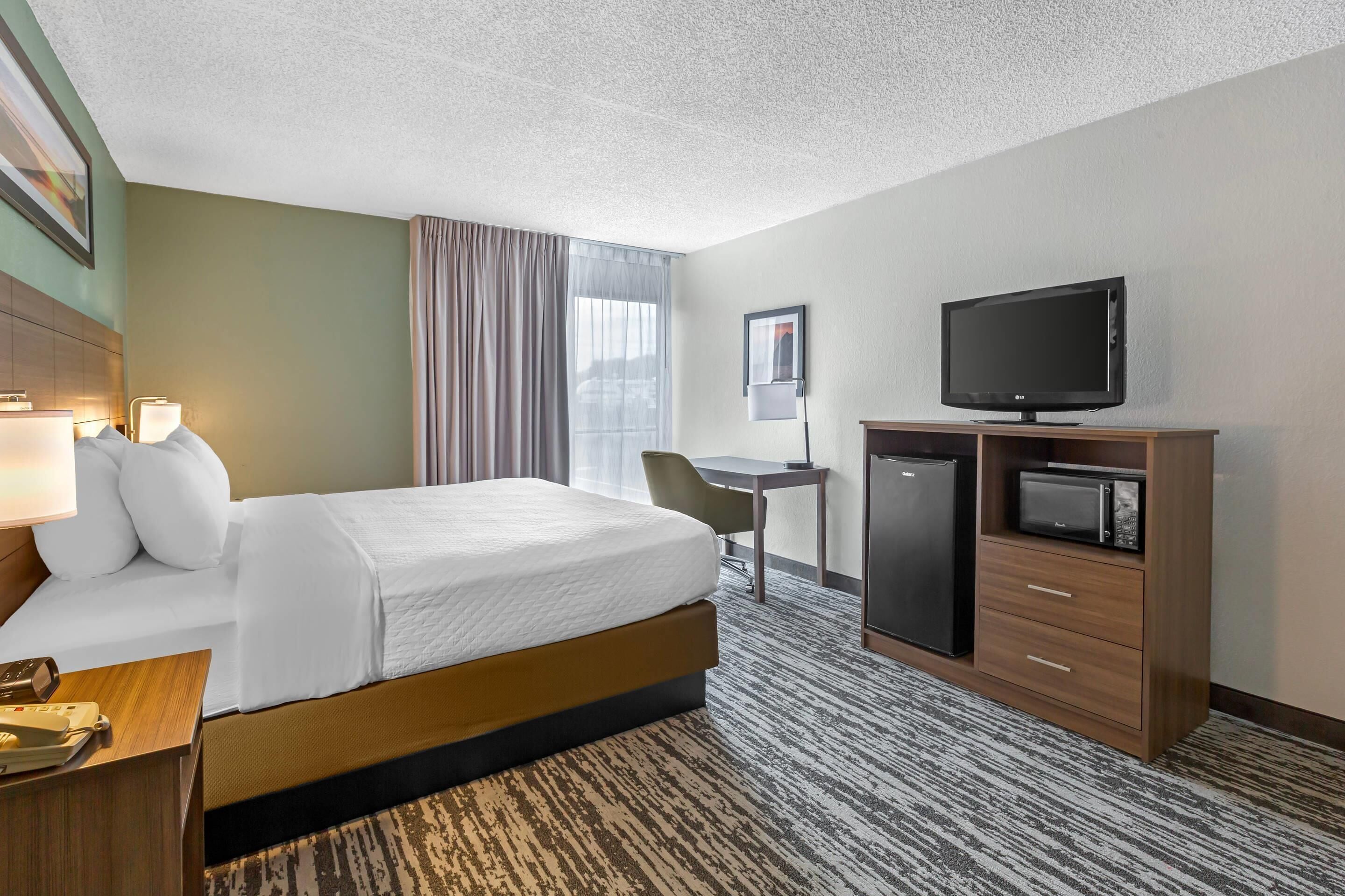 A hotel room with a bed, desk, television, and a refrigerator.