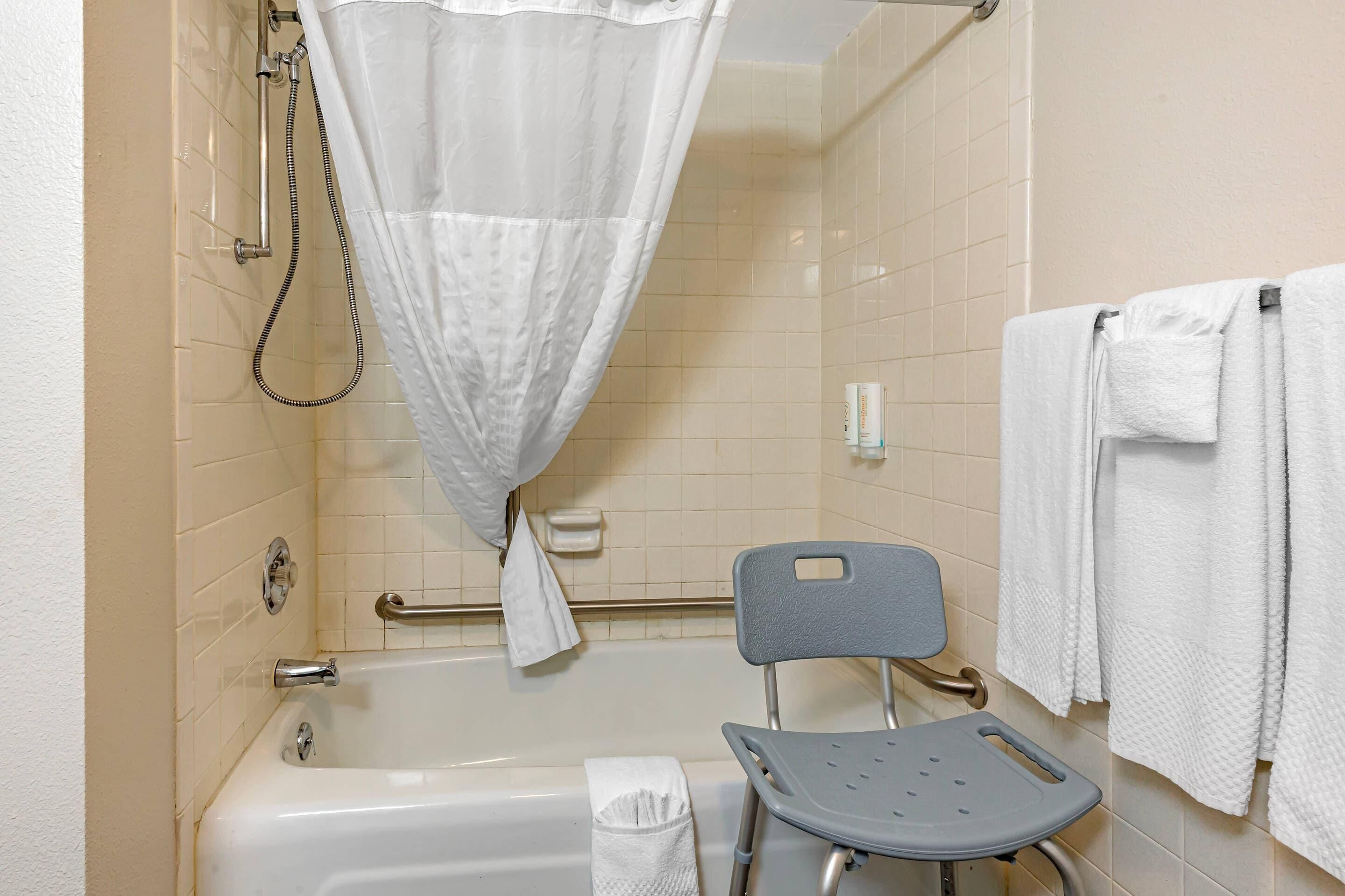 Un bagno con una vasca, una doccia, una maniglia di sostegno, una sedia e un porta asciugamani.