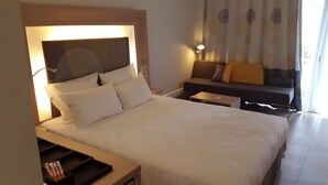 A hotel room with a large bed, bedside tables, a sofa, and a wall-mounted lamp. - Hôtel La Tchadienne (Ex Novotel) (N'Djamena)