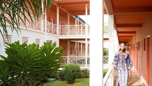 A hotel corridor with a covered outdoor area, a small garden, and a person in a patterned dress. - Hôtel La Tchadienne (Ex Novotel) (N'Djamena)