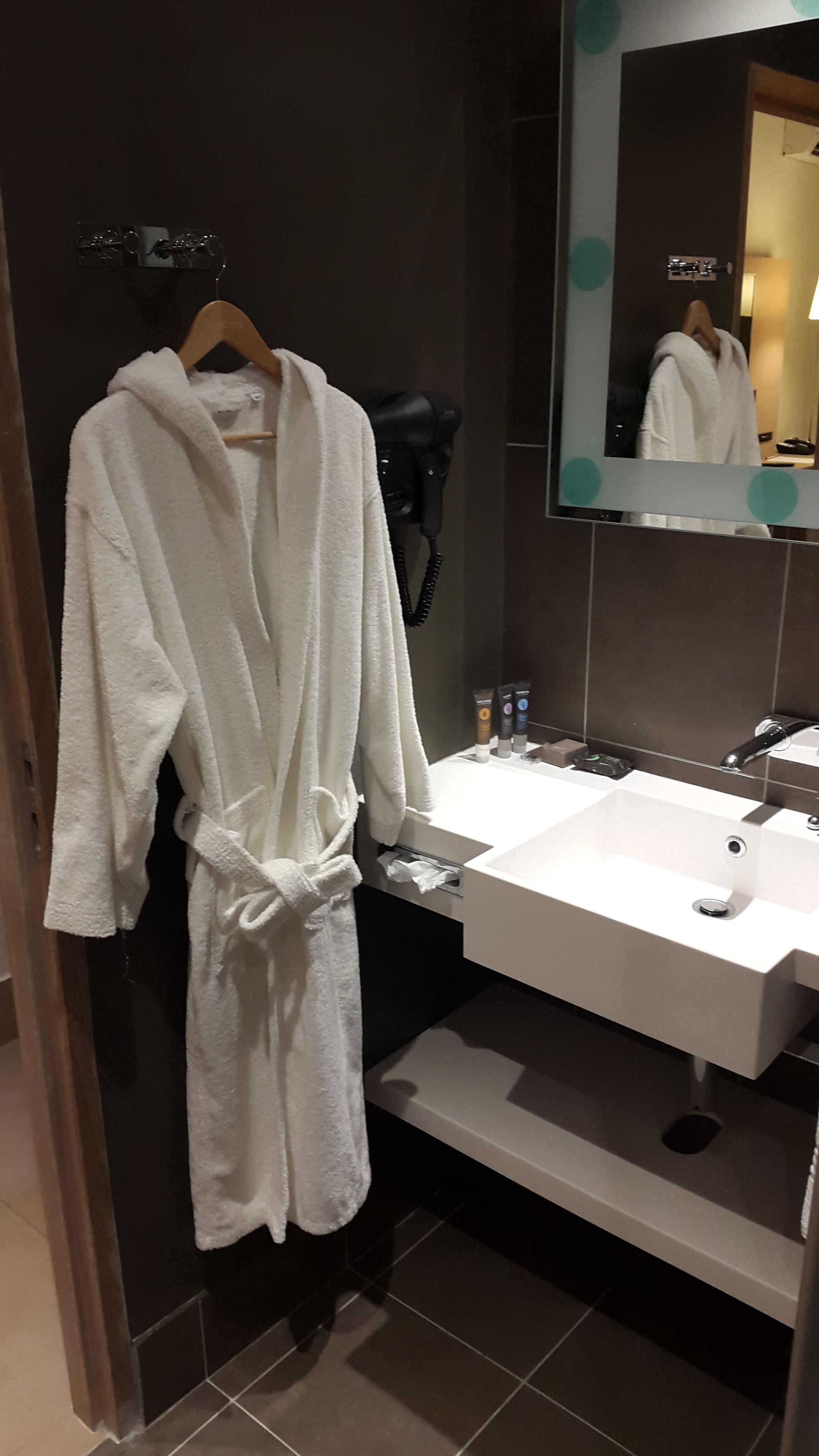 Un bagno con un lavandino bianco, uno specchio e un accappatoio appeso a un appendiabiti.