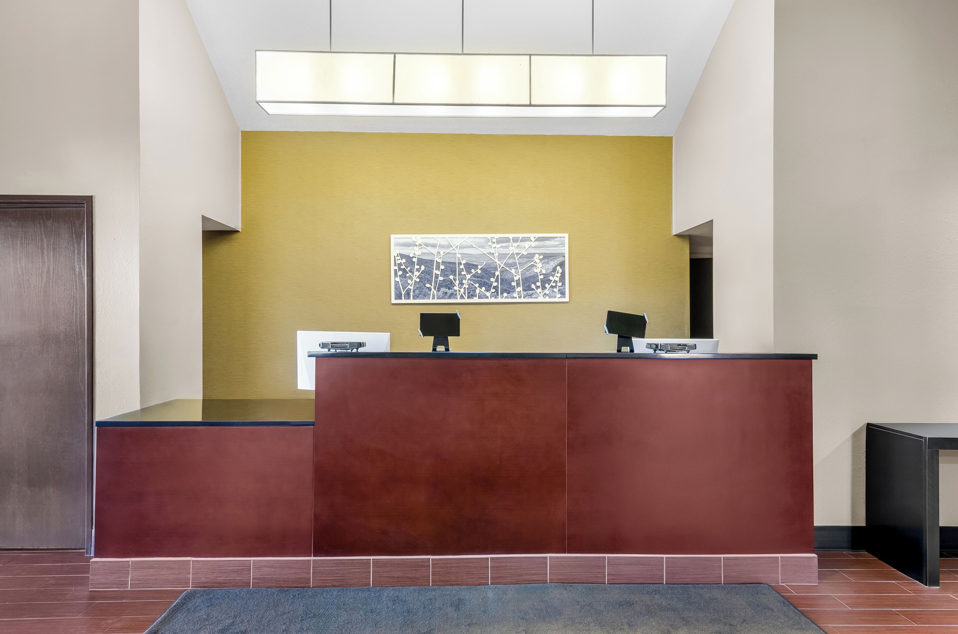 Un mostrador de recepción de diseño moderno, una pared de acento amarilla y una obra enmarcada sobre él.