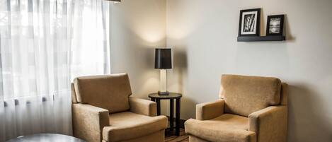 Habitación de hotel con dos sillones color beige, una mesa redonda pequeña, una lámpara y dos cuadros en la pared.