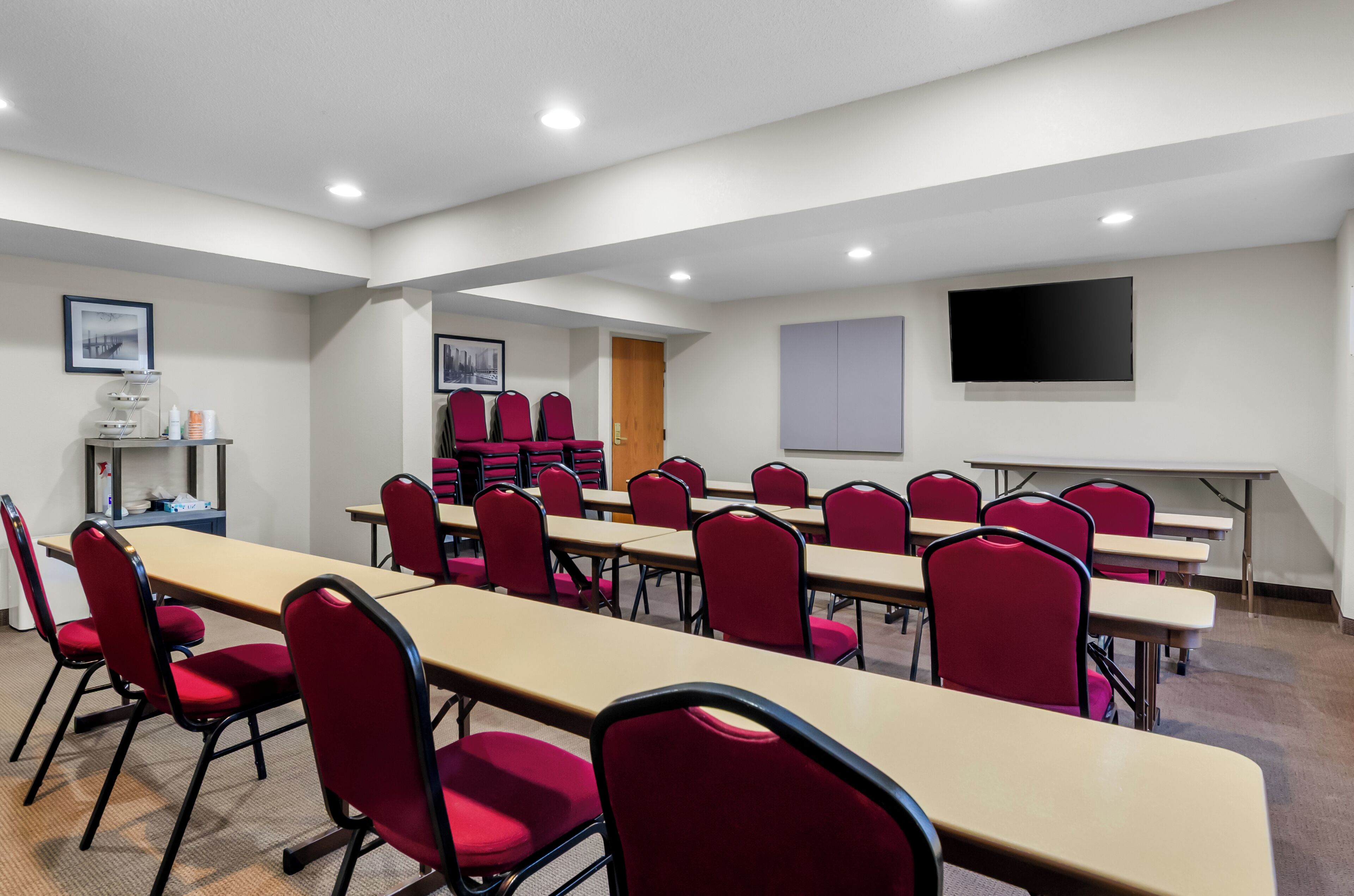 A conference room with long tables and red chairs, a projector screen, and a whiteboard on the wall.