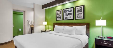 A hotel room with a large bed, a nightstand with a lamp, a green accent wall, and framed pictures above the bed.