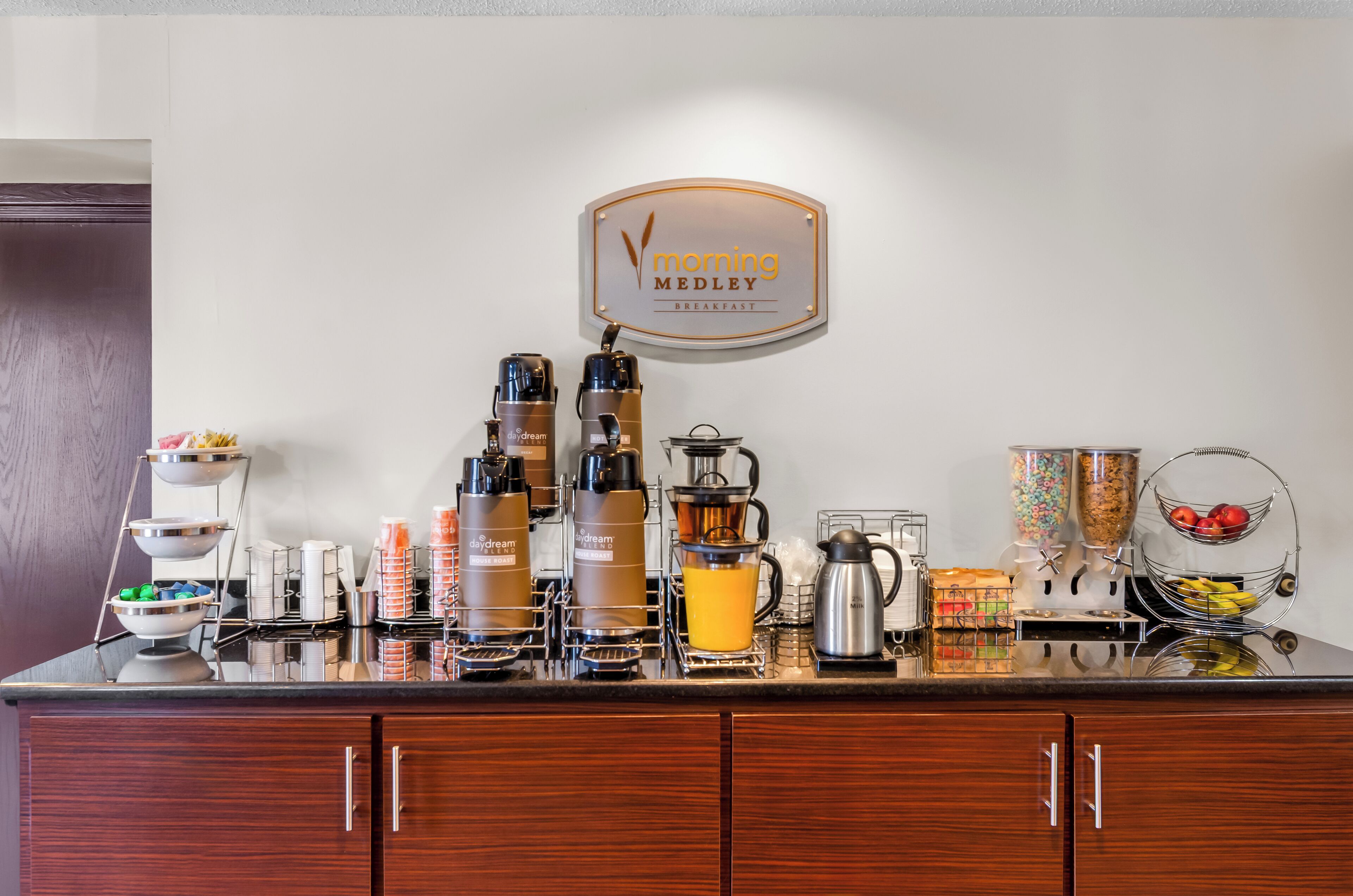 A breakfast bar with coffee makers, a coffee pot, and a fruit bowl.